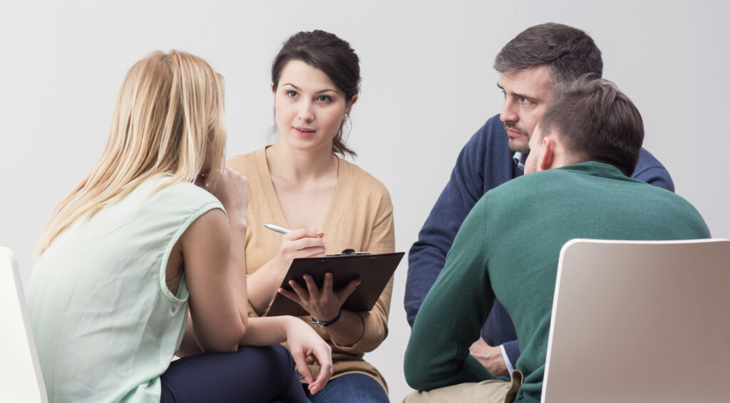 Das Bild zeigt eine Psychologin im Gespräch mit einer Therapiegruppe.